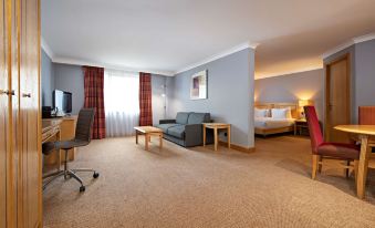 a hotel room with a bed , desk , couch , and television is shown with carpeted floor at DoubleTree by Hilton Swindon