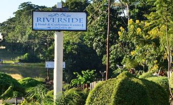 a signpost for riverside hotel & conference center , surrounded by trees and bushes , with a view of the river in the background at Riverside Apartments