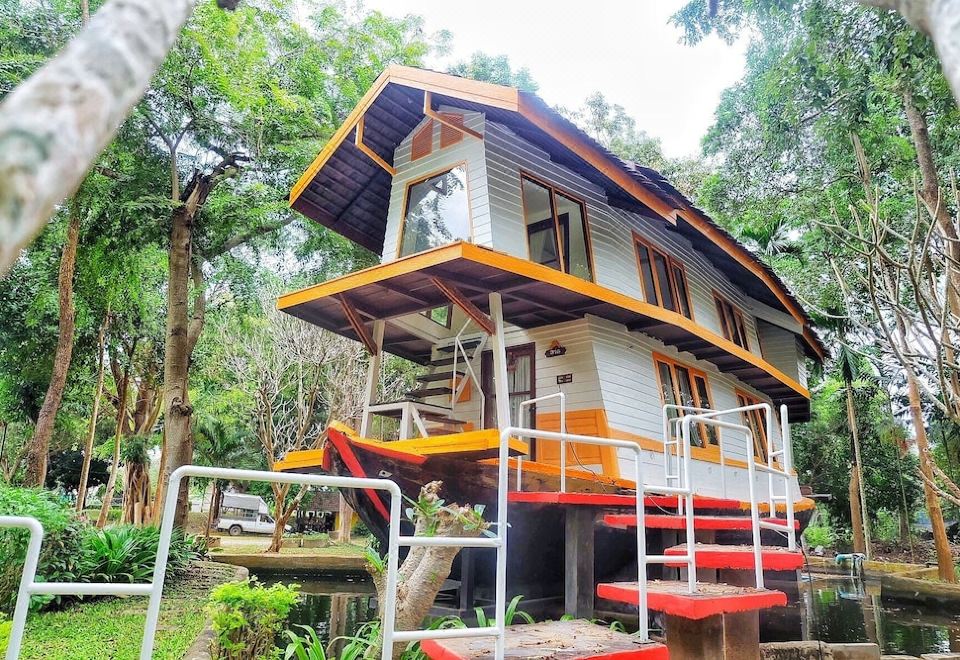 a small house with an orange and white exterior is situated in a forested area at Baanrai Riverkkwai Resort