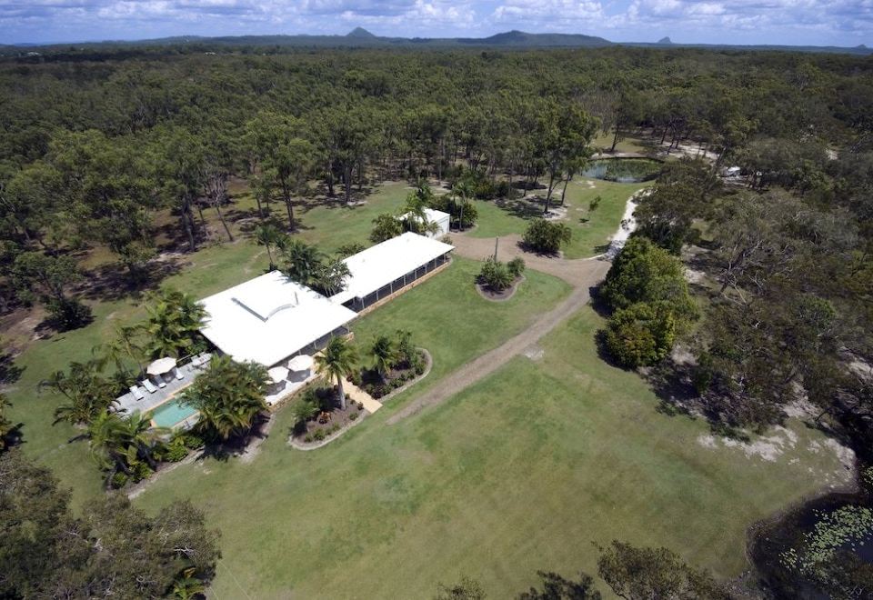 aerial view of a large white house surrounded by trees , with a swimming pool in the foreground at Noosa North Shore Retreat