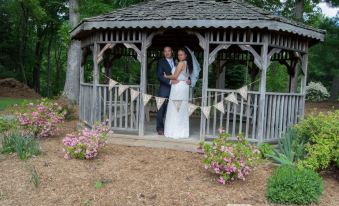 a newlywed couple stands in a gazebo surrounded by flowers , with the bride holding a bouquet of flowers at The Mountain Rose Inn