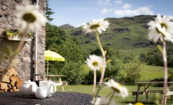 a patio with a table , chairs , and an umbrella is shown in front of a mountain landscape at YHA Eskdale