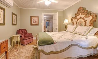 a large bed with a white and green comforter is in the middle of a room with a red chair , lamp , and chandelier at Broad River Inn
