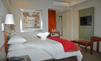 a large bed with a red blanket and white sheets is in a hotel room at Indaba Lodge Gaborone