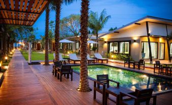 a large wooden deck with several lounge chairs and umbrellas surrounding a swimming pool , surrounded by palm trees at Aroonsawad Riverview Resort