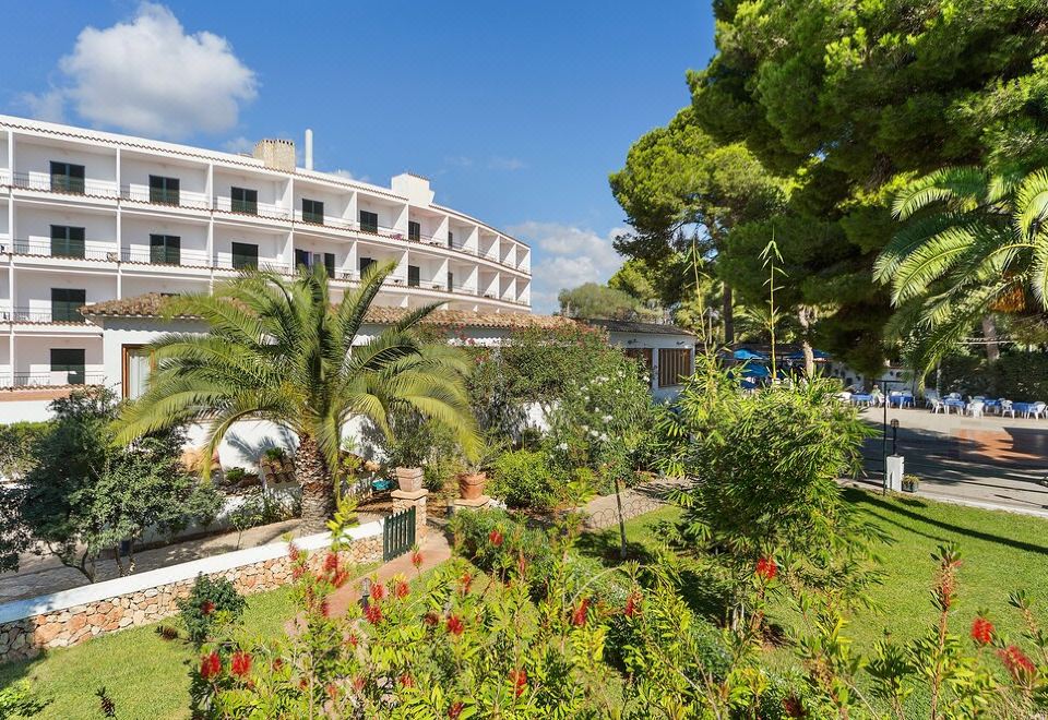 a large hotel surrounded by a lush garden , with several palm trees in the background at Hotel Cala Murada