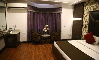 a modern hotel room with wooden flooring , white walls , and purple curtains , featuring a bed , chairs , table , and flowers at Jalandhar Shangrila Hotel