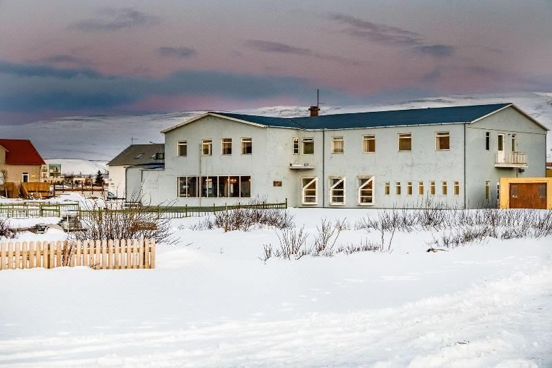a large white building surrounded by snow - covered ground , with a wooden fence in the foreground at Hotel Blonduos