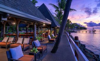 a waterfront restaurant with palm trees and chairs , set against a backdrop of the ocean at Shangri-La Yanuca Island, Fiji
