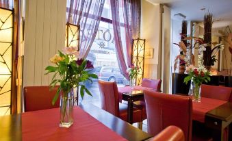 a cozy restaurant with red tables , chairs , and flowers in vases , along with a window that offers a view of the outside at Hotel Admiral