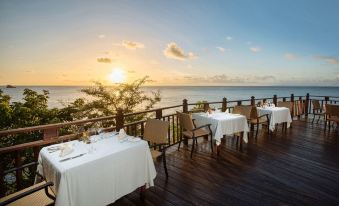 a wooden deck with tables and chairs set up for a dining experience , overlooking the ocean at Cap Maison Resort & Spa