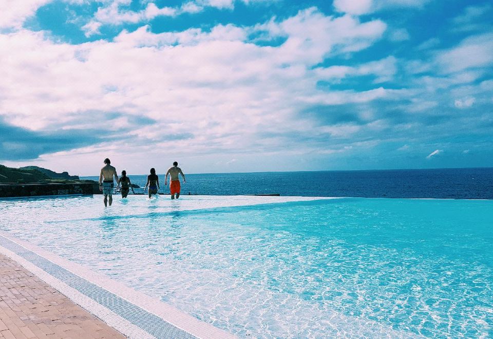 a group of people standing near a large body of water , possibly a pool or an ocean at Pedras do Mar Resort & Spa