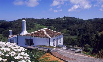 a white building with a pointed roof and chimney , situated on a hillside overlooking green hills and a clear blue sky at Hotel Colombo