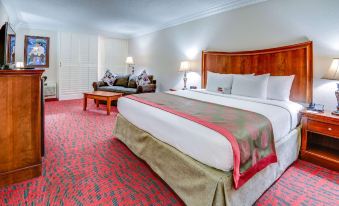 a large bed with a wooden headboard and white linens is in a hotel room with a red carpeted floor at Ramada by Wyndham Metairie New Orleans Airport