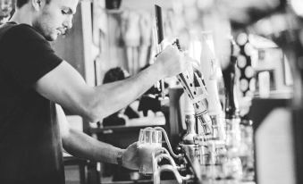 a black and white photo of a bartender pouring beer from a tap in a bar at The Brown Horse Inn