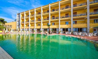 a large yellow building with balconies and a swimming pool in front of it , surrounded by palm trees at Grand Hotel Terme di Augusto