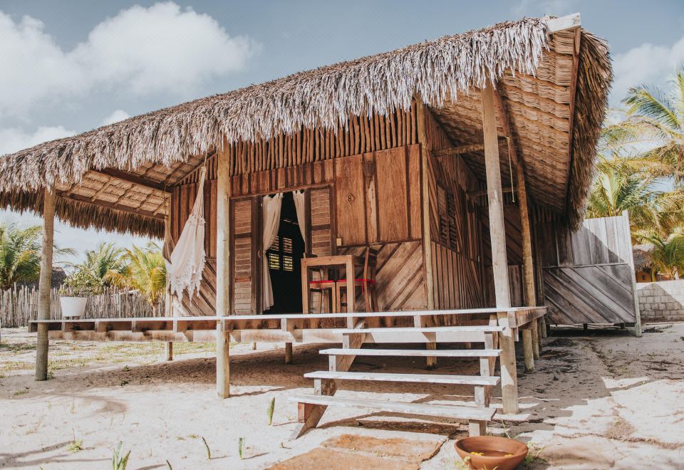 a wooden building with a thatched roof is surrounded by dirt and has a set of stairs leading up to it at Ventana Hotel