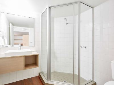 a modern bathroom with a walk - in shower , wooden floor , and white tiles on the walls at Ibis Melbourne Hotel and Apartments