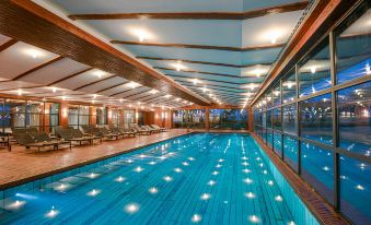 an indoor swimming pool surrounded by a wooden deck , with several lounge chairs placed around it at Lykia World Antalya - All Inclusive