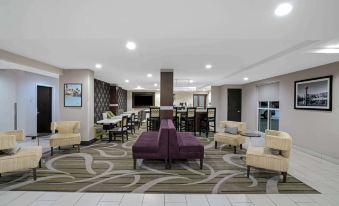 a large , well - lit room with a purple couch and chairs , white tables , and a bar area at La Quinta Inn & Suites by Wyndham Knoxville North I-75