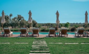 a backyard with a swimming pool surrounded by chairs and umbrellas , creating a relaxing atmosphere at Masseria le Fabriche