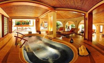 a luxurious indoor hot tub surrounded by wooden beams , with several lounge chairs placed around it at Tabacon Thermal Resort & Spa