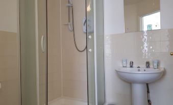 a modern bathroom with a glass shower door , white tiled walls , and a white sink at The Westgate