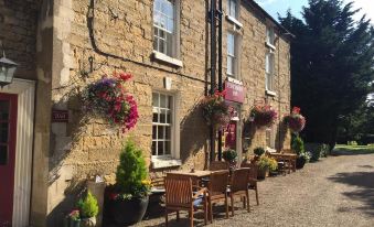 a stone building with flower pots hanging from the windows , and wooden tables and chairs outside at The Coachman Inn