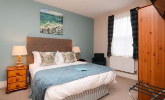 a cozy bedroom with a large bed , a window , and various items on the bedside table at St Andrews Town Hotel