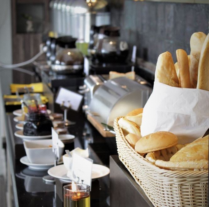 a dining table with a variety of food items , including bread , bowls , cups , and utensils at Horison Gkb Gresik