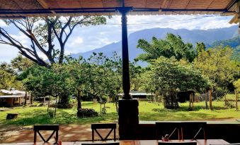 a wooden table with chairs is set up under a covered area with mountains in the background at Jungle Hut