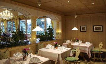 a restaurant with several tables and chairs , white tablecloths , and potted plants in the corner at Hotel Cristallo