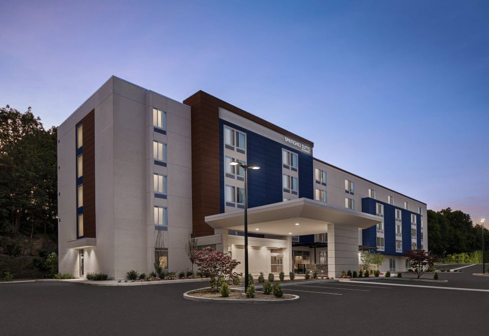 a modern hotel building with a large parking lot in front of it , surrounded by trees at SpringHill Suites Tuckahoe Westchester County