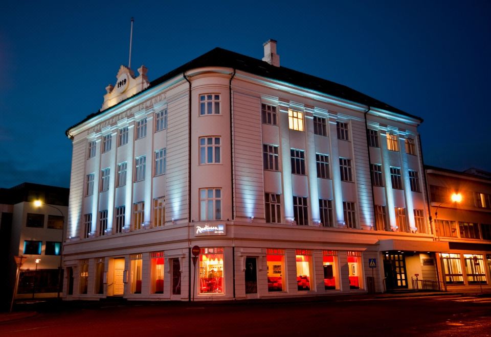 a large white building with blue lights shining on it , and a car parked in front of it at Radisson Blu 1919 Hotel Reykjavik