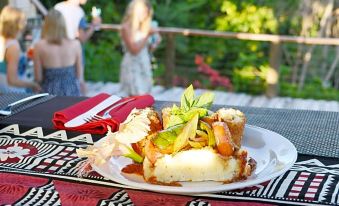 a plate of food is on a table with people in the background , and the person is holding a red napkin at Mantaray Island Resort