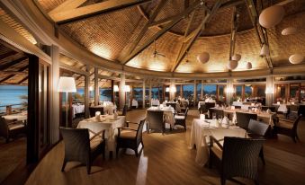 a large , circular restaurant with wooden tables and chairs is shown at night , illuminated by lights at Hilton Moorea Lagoon Resort and Spa