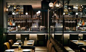 a dimly lit restaurant with wooden tables and chairs , a bar in the background , and multiple wine glasses hanging from the ceiling at Nohga Hotel Akihabara Tokyo