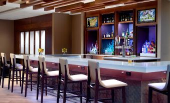 a well - equipped bar with various bottles and glasses , as well as several chairs and tables in the room at Atlanta Marriott Peachtree Corners