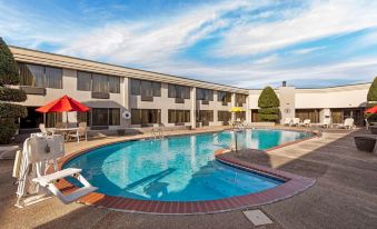 an outdoor swimming pool surrounded by a hotel , with several chairs and umbrellas placed around the pool area at Best Western Plus Madison-Huntsville Hotel