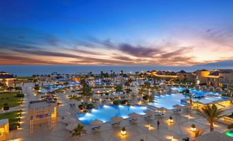 a large resort with a pool and multiple buildings is lit up at night , as the sky appears to be pink at Pickalbatros White Beach Taghazout - Adults Friendly 16 Years Plus - All Inclusive