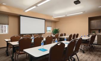 a conference room with rows of chairs arranged in a semicircle , and a projector screen on the wall at Hyatt House Minot