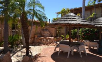 a patio with a table and chairs , a thatched umbrella , and palm trees in front of a house at The Lodge Motel