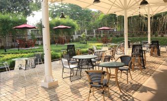 an outdoor dining area with multiple tables and chairs , surrounded by a lush green garden at Java Palace Hotel
