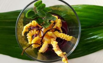 a small glass dish filled with a yellow and purple food item is placed on top of a green leaf at Hotel Capital