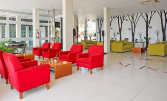 a modern , well - lit living room with red and green sofas , wooden tables , and a tree mural on the wall at Front One Resort Magelang