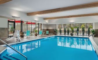 an indoor swimming pool surrounded by windows , with several lounge chairs placed around the pool area at Home2 Suites by Hilton Long Island Brookhaven