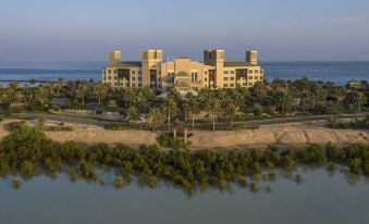 a large , modern hotel complex situated near the water 's edge , with trees and buildings surrounding it at Anantara Desert Islands Resort & Spa