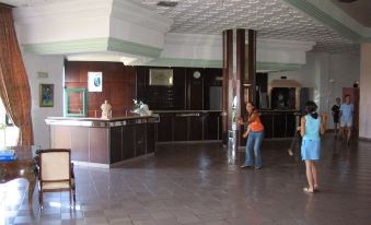 a hotel lobby with two people standing at the reception desk and a woman walking towards them at Royal Golf