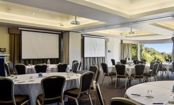 a large conference room with multiple tables and chairs , a projector screen , and a view of the outdoors at O'Reilly's Rainforest Retreat