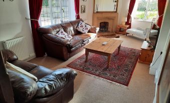a spacious living room with a brown leather couch , a wooden coffee table , and a rug on the floor at The White Cottage